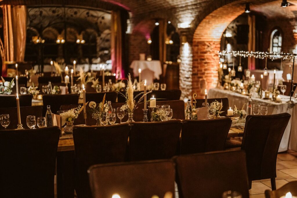 Ein abgedunkelter Raum mit einem stimmungvollen warmen Licht durch Lichterketten und gedeckte lange Tische.